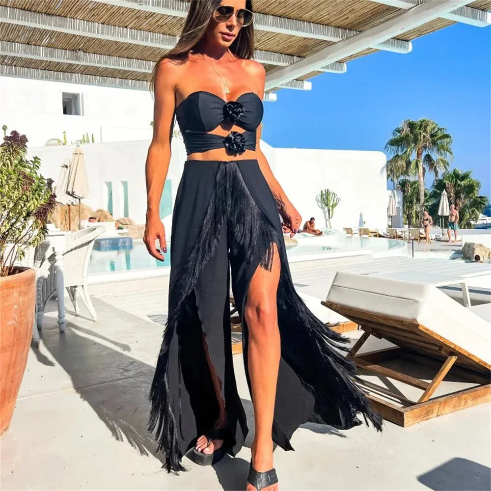Woman in a black strapless top and long black skirt with fringe, standing on a sunlit patio.
